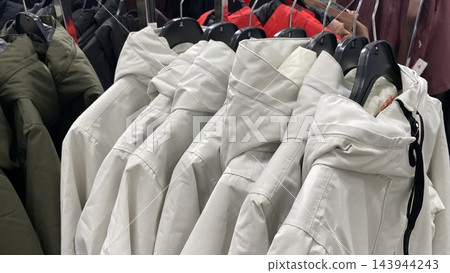 White winter jackets with hoods hanging on clothing rack in second hand store White winter jackets with hoods hanging on clothing rack in second hand store 143944243
