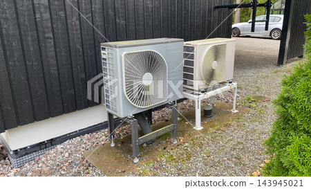 Outdoor heat pump units installed beside residential house for energy efficient heating and cooling system Outdoor heat pump units installed beside residential house for energy efficient heating and cooling system 143945021