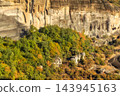 Meteora Greece massive rock cliff autumn forest with green and yellow foliage under sunlight 143945163