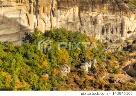 Meteora Greece massive rock cliff autumn forest with green and yellow foliage under sunlight Meteora Greece massive rock cliff autumn forest with green and yellow foliage under sunlight 143945163