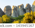Meteora Greece massive rock pillars glowing in sunset light behind green trees 143945167