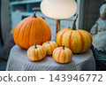 striped orange pumpkins on textured fabric near glowing round lamp, cozy fall indoor decoration featuring seasonal harvest squash under warm lighting 143946772
