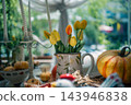 yellow tulips inside vintage pitcher near striped pumpkin, cozy autumn harvest decoration featuring floral arrangement and tall candles indoors 143946838