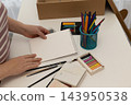 Woman preparing to paint at a tidy home desk with art supplies and notebook 143950538