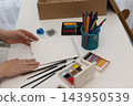 Woman arranging brushes and art supplies at a bright white craft desk for mindful analogue art 143950539
