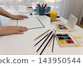 Woman painting with watercolors at home in natural daylight, hands on drawing pad 143950544