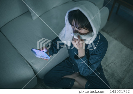 夜裡,一位女子頭上裹著毛巾,正在看著她的智慧型手機。 夜裡,一位女子頭上裹著毛巾,正在看著她的智慧型手機。 143951732
