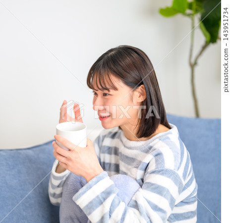 一位年輕女子正放鬆地躺在沙發上喝飲料。 一位年輕女子正放鬆地躺在沙發上喝飲料。 143951734