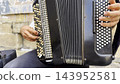 Male hands of musician playing the accordion at urban street. The detailed view highlights texture of instrument, capturing rhythm, tradition, and the expressive character of live music performance 143952581