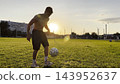 Young man juggling soccer ball on stadium at sunset. Professional footballer kicking ball at green field. Sportsman practicing tricks at meadow with sunlight at background. Freestyle football 143952637