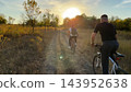Young male friends ride mountain ski bikes along trail on sunny summer day. Beautiful golden sunlight at background. Concept of active lifestyle, adventure spirit and carefree weekend outdoor 143952638