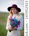 Woman holding a colorful bouquet while wearing a stylish hat in a peaceful outdoor setting during daylight 143952923