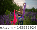 Woman dancing with colorful scarves in a vibrant flower field during a sunny day 143952924