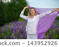 Woman enjoying a purple scarf in a lush field of blooming flowers during a sunny day 143952926