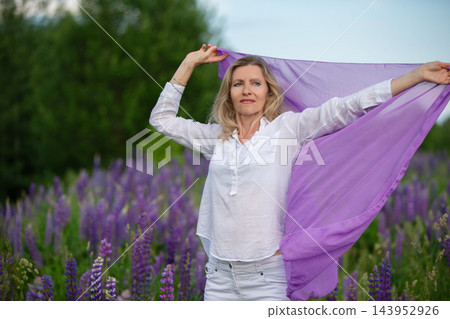 Woman enjoying a purple scarf in a lush field of blooming flowers during a sunny day Woman enjoying a purple scarf in a lush field of blooming flowers during a sunny day 143952926