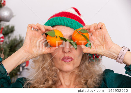 An elderly woman in a Christmas hat with a playful expression holds oranges above her eyes during Christmas An elderly woman in a Christmas hat with a playful expression holds oranges above her eyes during Christmas 143952930