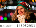 Elderly woman wearing party hat and white scarf with bokeh lights in background at night 143952931
