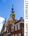 Vertical coastal digital publication of town hall clock tower historic architecture traditional Dutch brick houses blue sky Veere Zeeland Netherlands European travel maritime heritage commercial 143954417