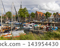 Horizontal perspective of town hall clock tower harbor marina sailboats traditional Dutch brick houses wooden posts blue sky Veere Zeeland Netherlands European travel commercial 143954430