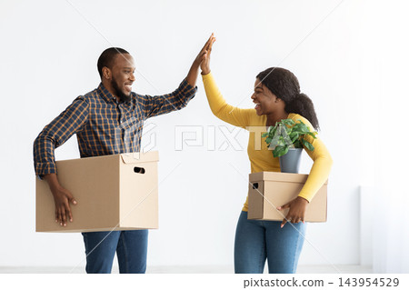 Happy Moving Day. Joyful Black Spouses Holding Cardboard Boxes And Giving High Five To Each Other, Cheerful African American Couple Celebrating Relocation To Their Own Apartment, Copy Space Happy Moving Day. Joyful Black Spouses Holding Cardboard Boxes And Giving High Five To Each Other, Cheerful African American Couple Celebrating Relocation To Their Own Apartment, Copy Space 143954529