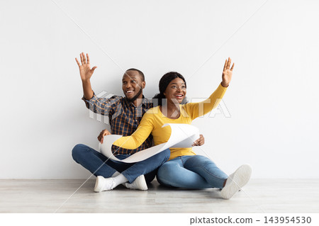 Happy Black Couple Sitting On Floor In New Flat, Holding Blueprints And Discussing Interior Design, Excited Young African American Spouses With Building Plan Imagining Style Of Their Apartment Happy Black Couple Sitting On Floor In New Flat, Holding Blueprints And Discussing Interior Design, Excited Young African American Spouses With Building Plan Imagining Style Of Their Apartment 143954530