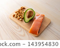 Protein diet and healthy fat concept. Salmon fillet, half of avocado and mixed nuts on cutting board on wooden kitchen table, closeup. 143954830