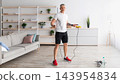 Male fitness and sporty lifestyle. Mature man exercising with jumping rope in living room at home. Morning physical training routine with skipping rope, free space 143954834