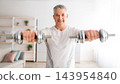 Athletic mature man lifting dumbells up, doing workout on arms strength, looking at camera and smiling, training at home in living room interior, panorama 143954840