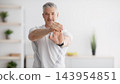 Mature man stretching hands, exercising at home, panorama with free space, selective focus. Aged man doing flexibility exercises, warming up for domestic training during covid 143954851