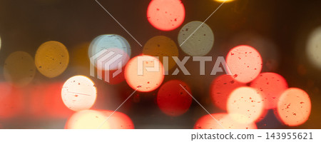 Abstract blurred lights create colorful bokeh circles in red, orange, white and blue against dark evening background. Soft glowing highlights suggest traffic, nightlife and urban motion at night 143955621