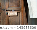 A beautifully framed, close-up shot captures a timeless scene centered on a rustic wooden door bearing a hand-hung "OPEN" sign. The composition utilizes a shallow depth of field, keeping the focus 143956600
