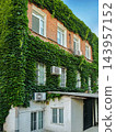 The courtyard side of three-story brick house is overgrown with ivy 143957152