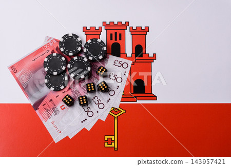 Playing cards, dice and chips on a Gibraltar flag, a gambling game of poker, blackjack or baccarat Playing cards, dice and chips on a Gibraltar flag, a gambling game of poker, blackjack or baccarat 143957421