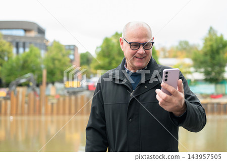 Senior Scandinavian Man Using Smartphone Near Urban Development Site in Turku Finland Senior Scandinavian Man Using Smartphone Near Urban Development Site in Turku Finland 143957505