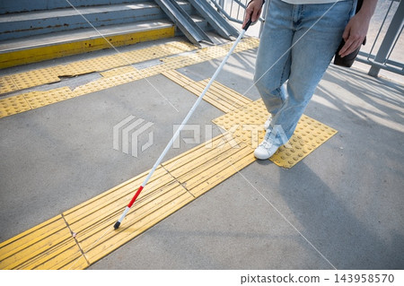 A blind woman walks using a cane and tactile tiles. A blind woman walks using a cane and tactile tiles. 143958570