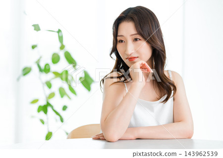 一張美麗的女子照片,她坐在桌旁,一手托著下巴。 一張美麗的女子照片,她坐在桌旁,一手托著下巴。 143962539