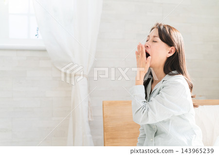 Woman yawning in bed after waking up Woman yawning in bed after waking up 143965239