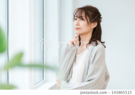 A woman by the window, thinking with her finger on her chin. A woman by the window, thinking with her finger on her chin. 143965515