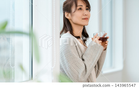 A woman sitting by the window with a cup of tea. 143965547