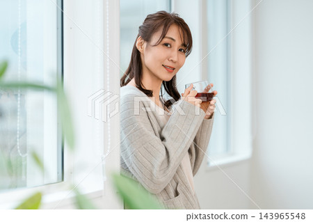 A woman in loungewear smiles, holding a cup of tea. 143965548