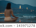 Woman meditating on beach shoreline with sea waves and Lady Buddha in Da Nang, Female practicing mindfulness by ocean at sunset with coastal mountains 143971278