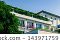 white hotel building featuring colorful balconies plus green roof garden, tropical resort facade with bright shutters lush vegetation under clear blue sky 143971759