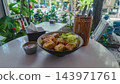 fried tofu and noodles with fresh green salad in ceramic bowl, healthy vegetarian lunch featuring asian street food outdoor on white table 143971761