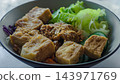close up of fried tofu with roasted peanuts and fresh green salad in bowl, macro view showing crispy asian vegetarian meal featuring sliced cucumber 143971769