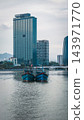traditional wooden fishing boats on river near modern city skyline, blue vessels moored inside urban bay against towering glass skyscrapers of Danang 143971770