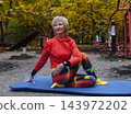 Mature woman practicing yoga and stretching outdoors in an autumn park. Active senior enjoying healthy aging, fitness, and vitality through outdoor workout and mindfulness. 143972202