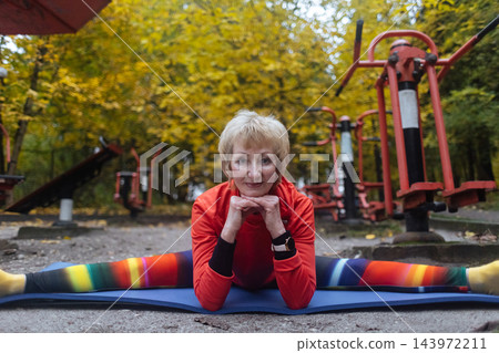 Mature woman practicing yoga and stretching outdoors in an autumn park. Active senior enjoying healthy aging, fitness, and vitality through outdoor workout and mindfulness. 143972211