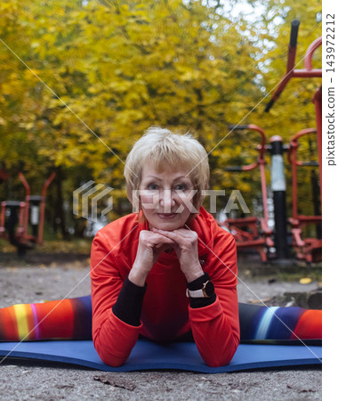 Mature woman practicing yoga and stretching outdoors in an autumn park. Active senior enjoying healthy aging, fitness, and vitality through outdoor workout and mindfulness. 143972212