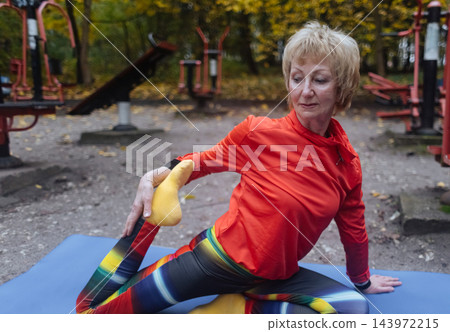 Mature woman practicing yoga and stretching outdoors in an autumn park. Active senior enjoying healthy aging, fitness, and vitality through outdoor workout and mindfulness. 143972215