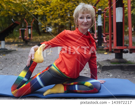 Mature woman practicing yoga and stretching outdoors in an autumn park. Active senior enjoying healthy aging, fitness, and vitality through outdoor workout and mindfulness. Mature woman practicing yoga and stretching outdoors in an autumn park. Active senior enjoying healthy aging, fitness, and vitality through outdoor workout and mindfulness. 143972217